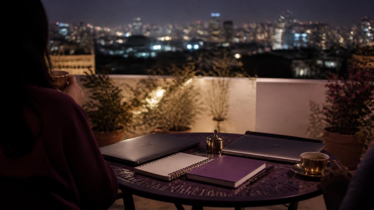 Two closed laptops and filter coffee on a rooftop table with city lights behind