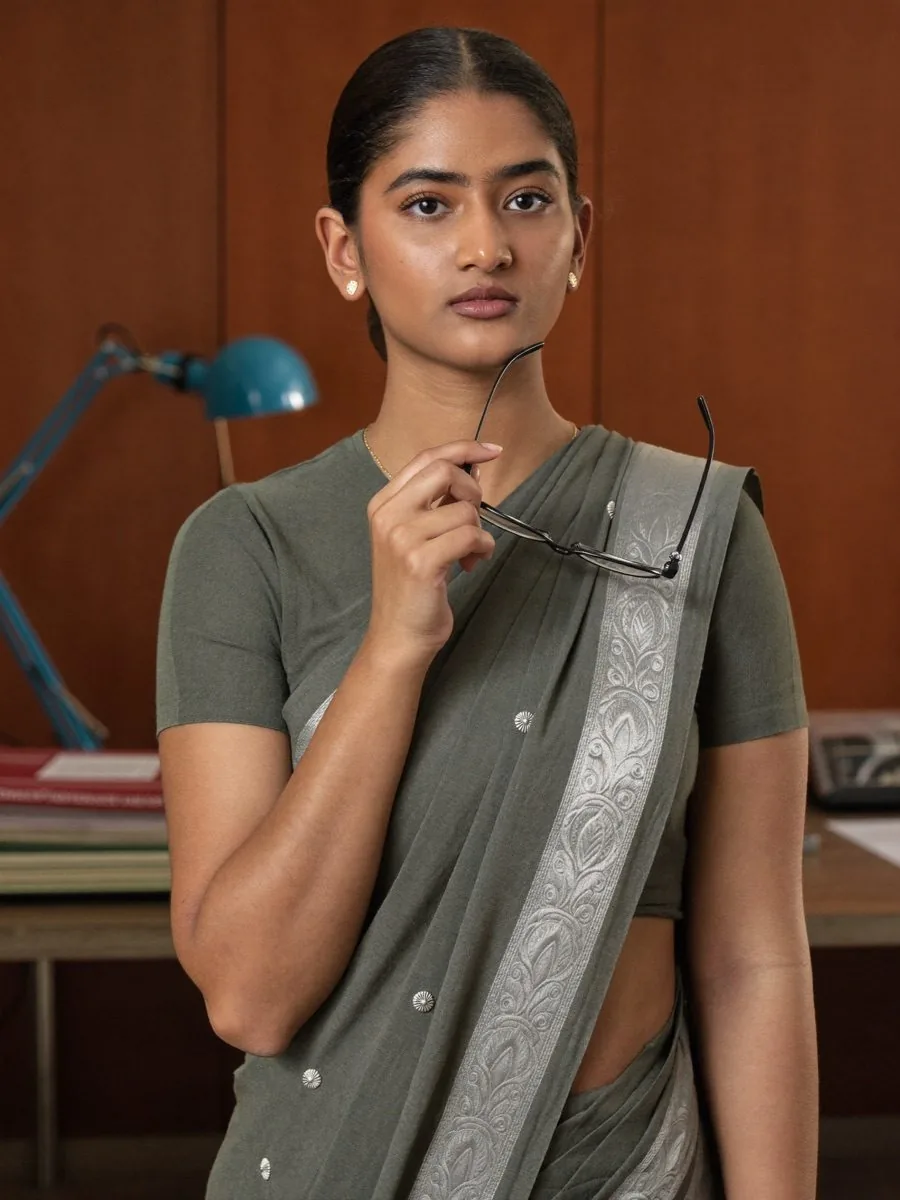 A thoughtful woman in a grey sari holding her glasses in a study
