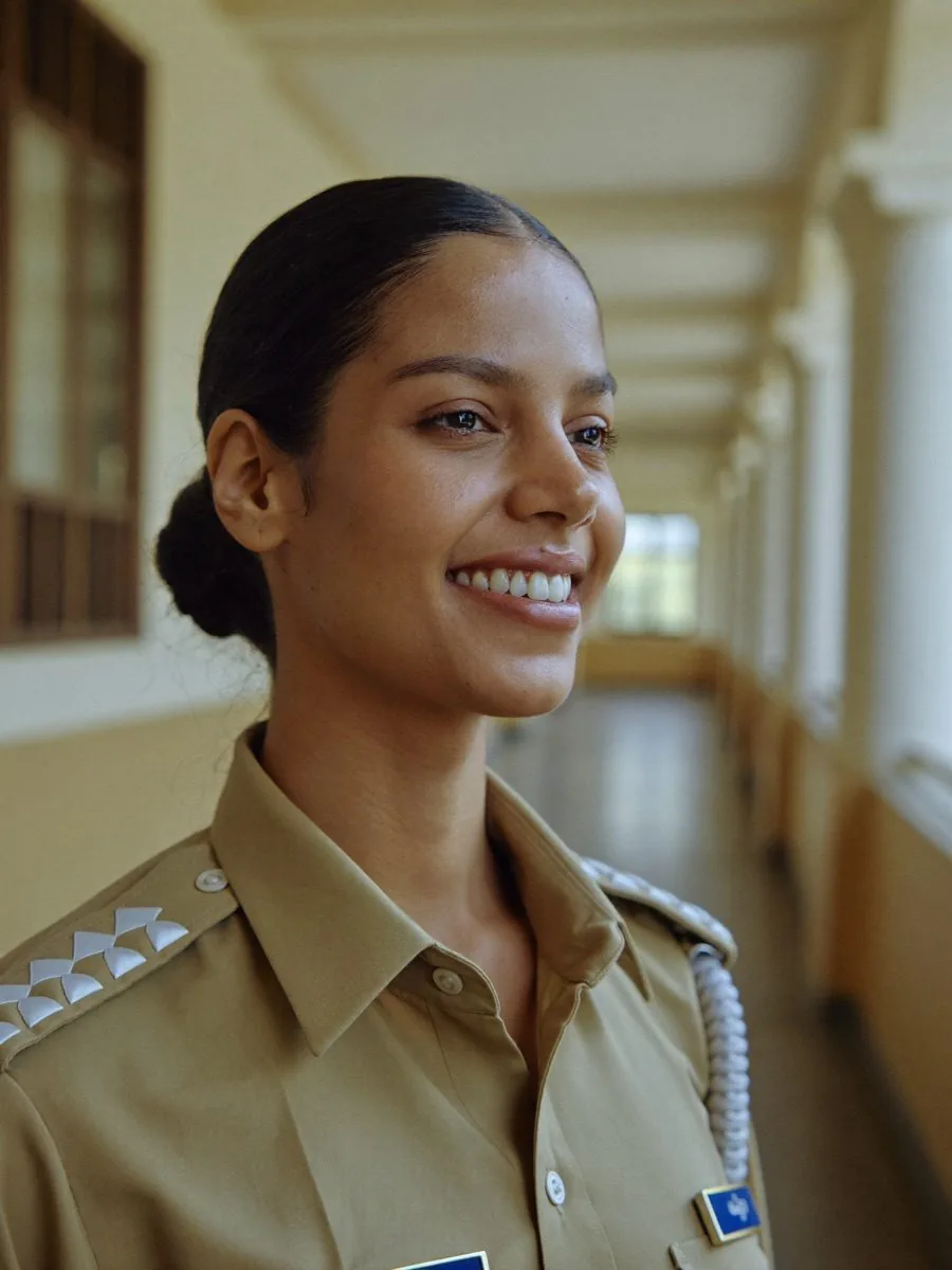 A smiling police officer in uniform in a sunlit corridor