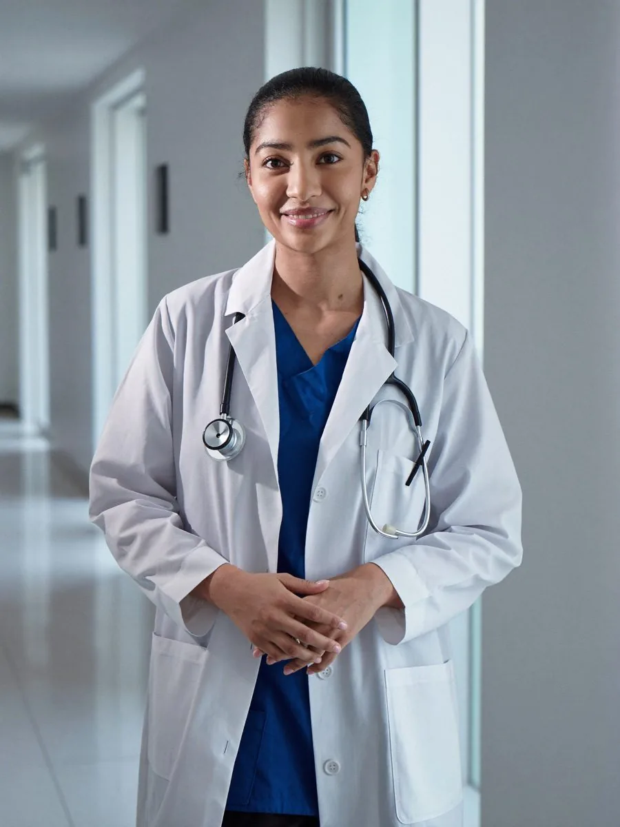 A smiling doctor in a white coat with a stethoscope in a hospital corridor
